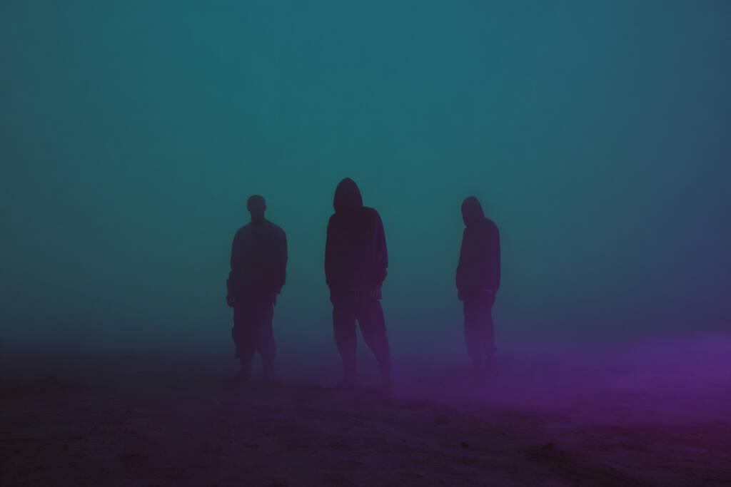 Three shadowed figures standing in neon mist — Bleed Electric band photo.