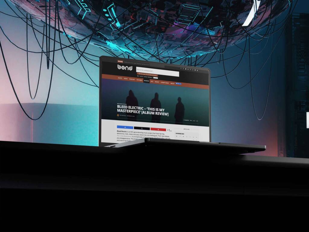 Laptop on a dark desk showing The Word Is Bond review of Bleed Electric's album "This Is My Masterpiece", with glowing sci-fi cables and a suspended tech sphere in the background.